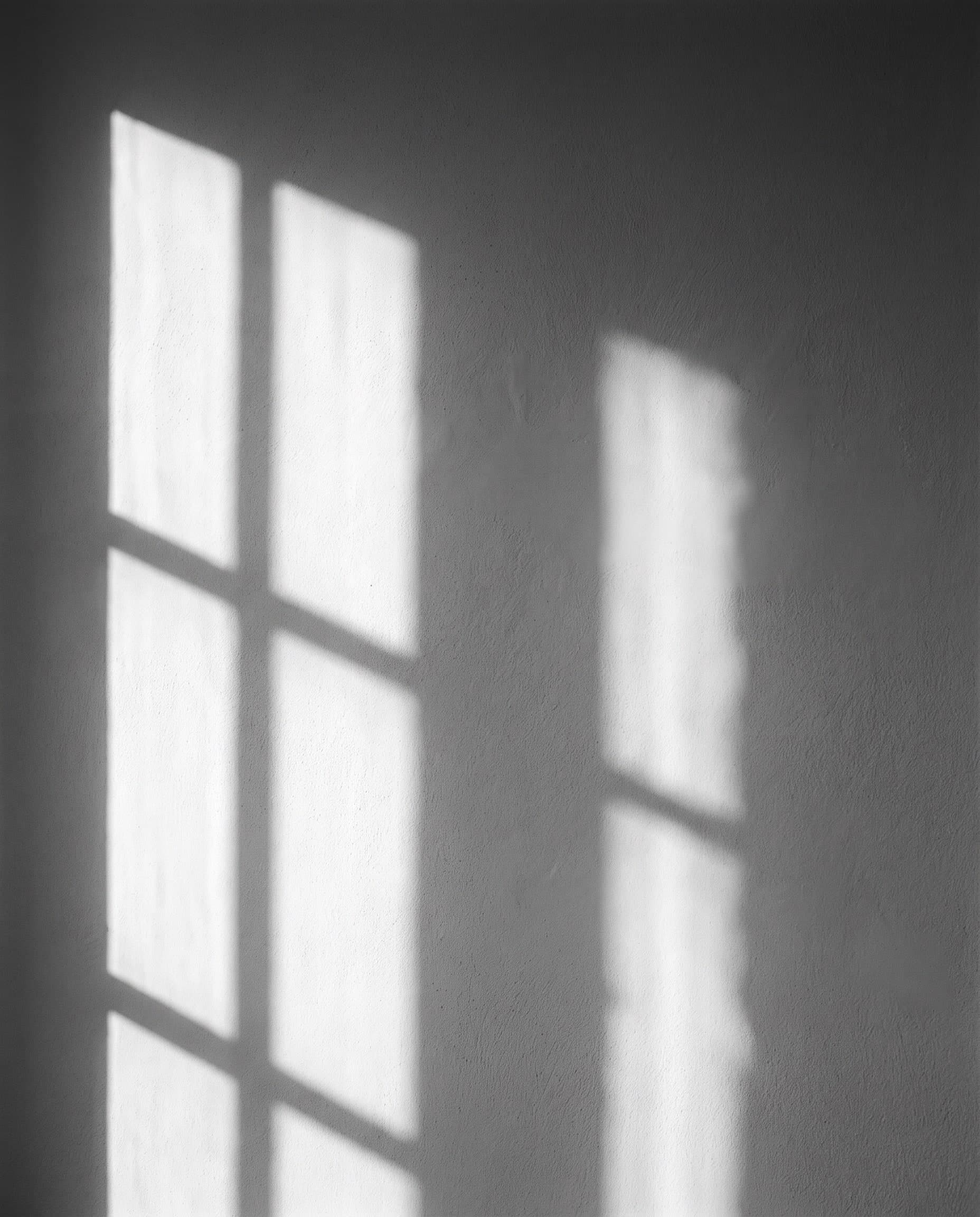 Schatten eines Sprossenfensters auf heller Putzwand, schwarzweiß